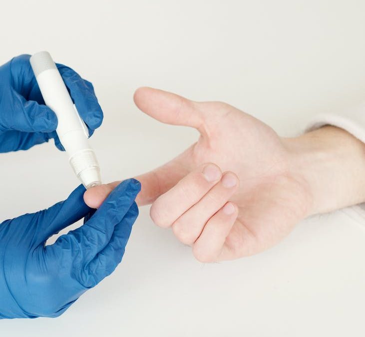 person in blue gloves using a lancet pen on a diabetic person